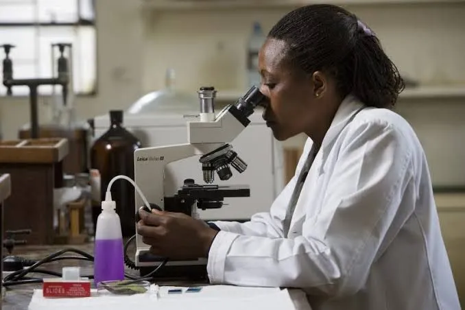 Woman in a white coat looking through a microscope